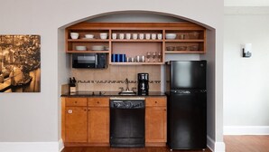 A compact kitchen with wooden cabinets, a black dishwasher, a black refrigerator, a microwave, and a coffee maker. - Getaway on the Riverwalk @ Riverside Suites- 1 Br Condo (San Antonio)
