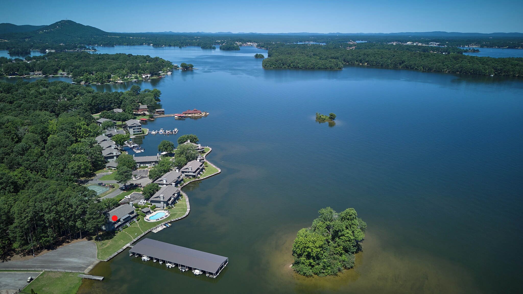 Vue aérienne d’une propriété au bord du lac, avec un port de plaisance, plusieurs bâtiments et un grand arbre près de l’eau.