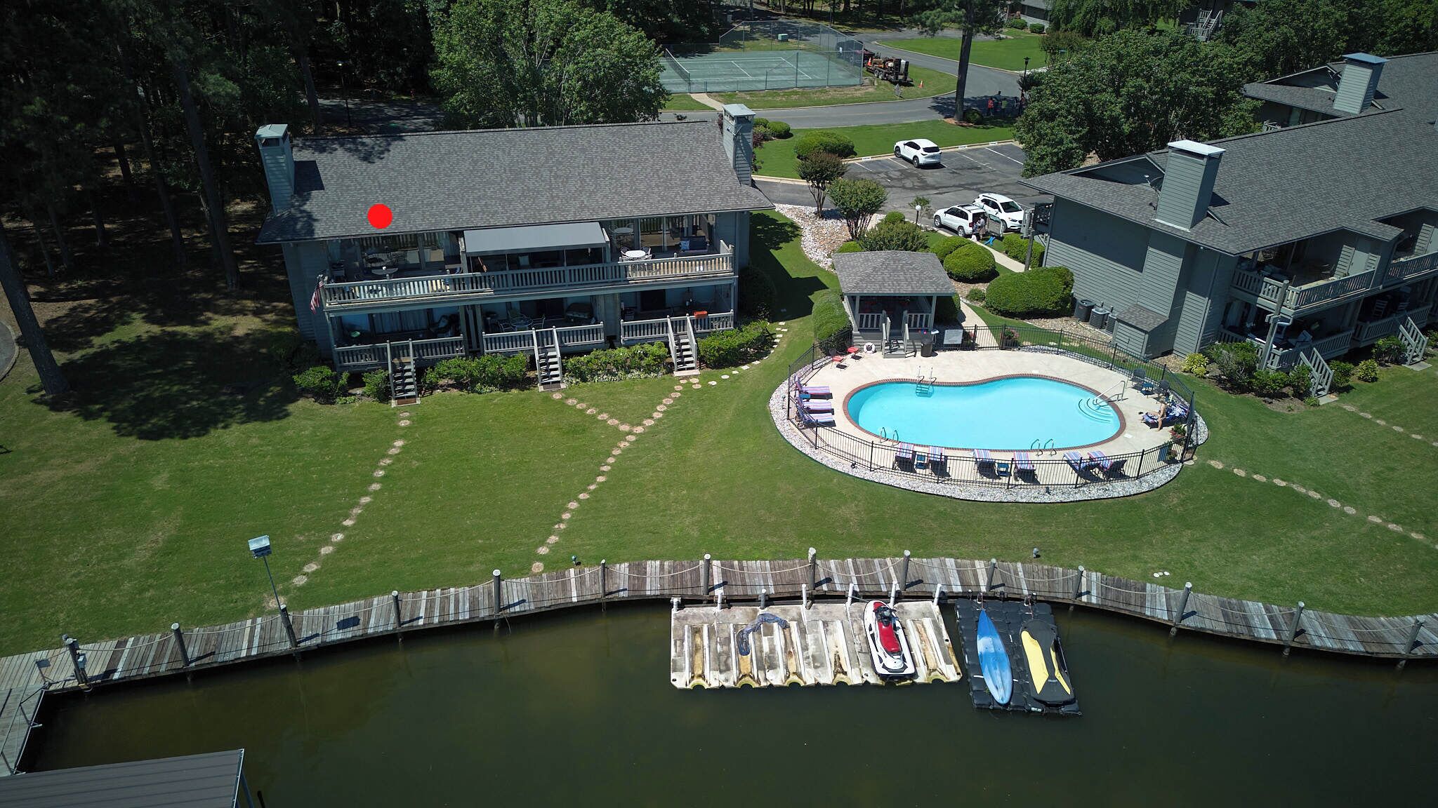 Una amplia casa con piscina, un muelle con kayaks y una cancha de tenis.