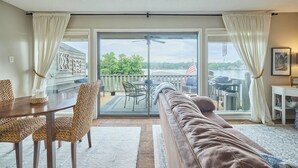 Ein großzügiger Wohnbereich mit einer Schiebeglasdoor zum Patio, einem braunen Sofa, einem Esstisch mit Korbstühlen und einem kleinen weißen Tisch mit einem gerahmten Bild.