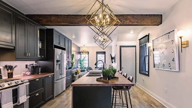 A modern kitchen with dark cabinets, stainless steel appliances, a central island with stools, and a chandelier.