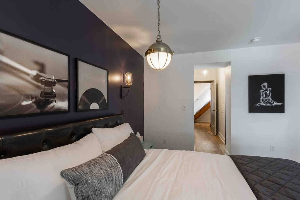 A modern bedroom with a large bed, a dark headboard, and a hanging light fixture.