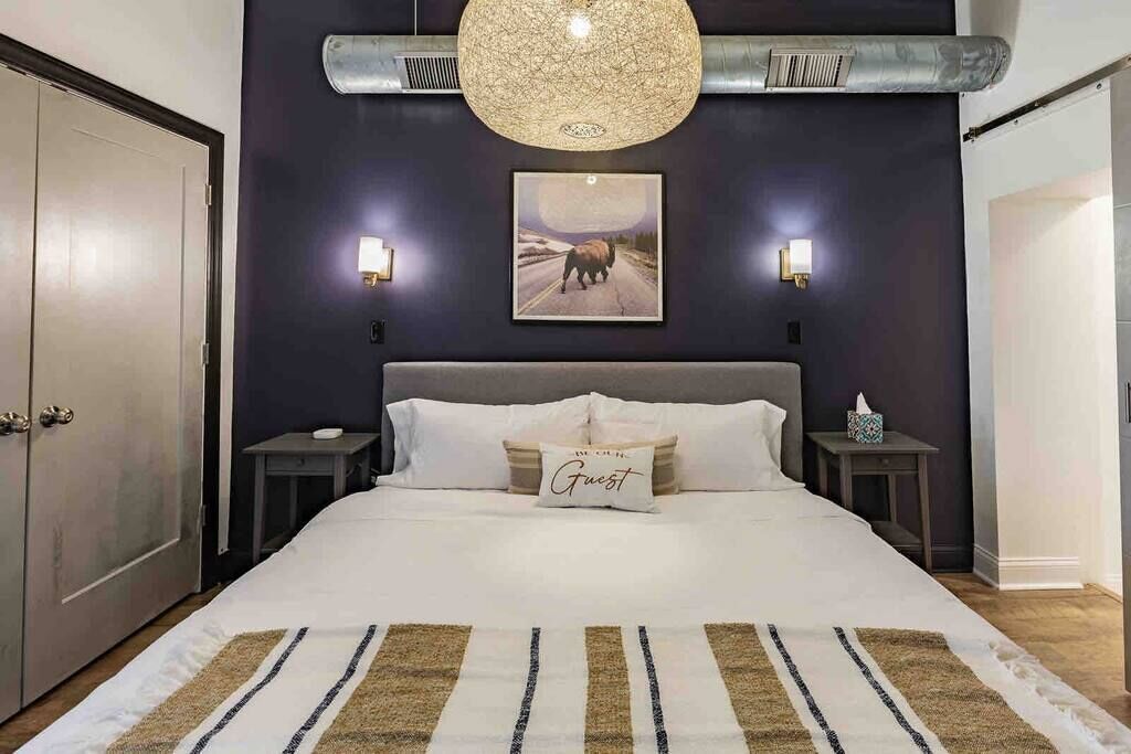 A bedroom with a large bed, a dark wall, a picture of a bull, and two bedside tables with lamps.