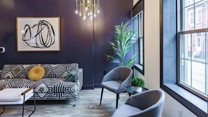 A modern living room with a geometric-patterned sofa, a grey armchair, and a large window with a view of the street.