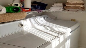 A front-loading white washer and dryer in a laundry room with a shelf above containing folded towels and laundry supplies. - The Ivy of Dresden (Dresden)