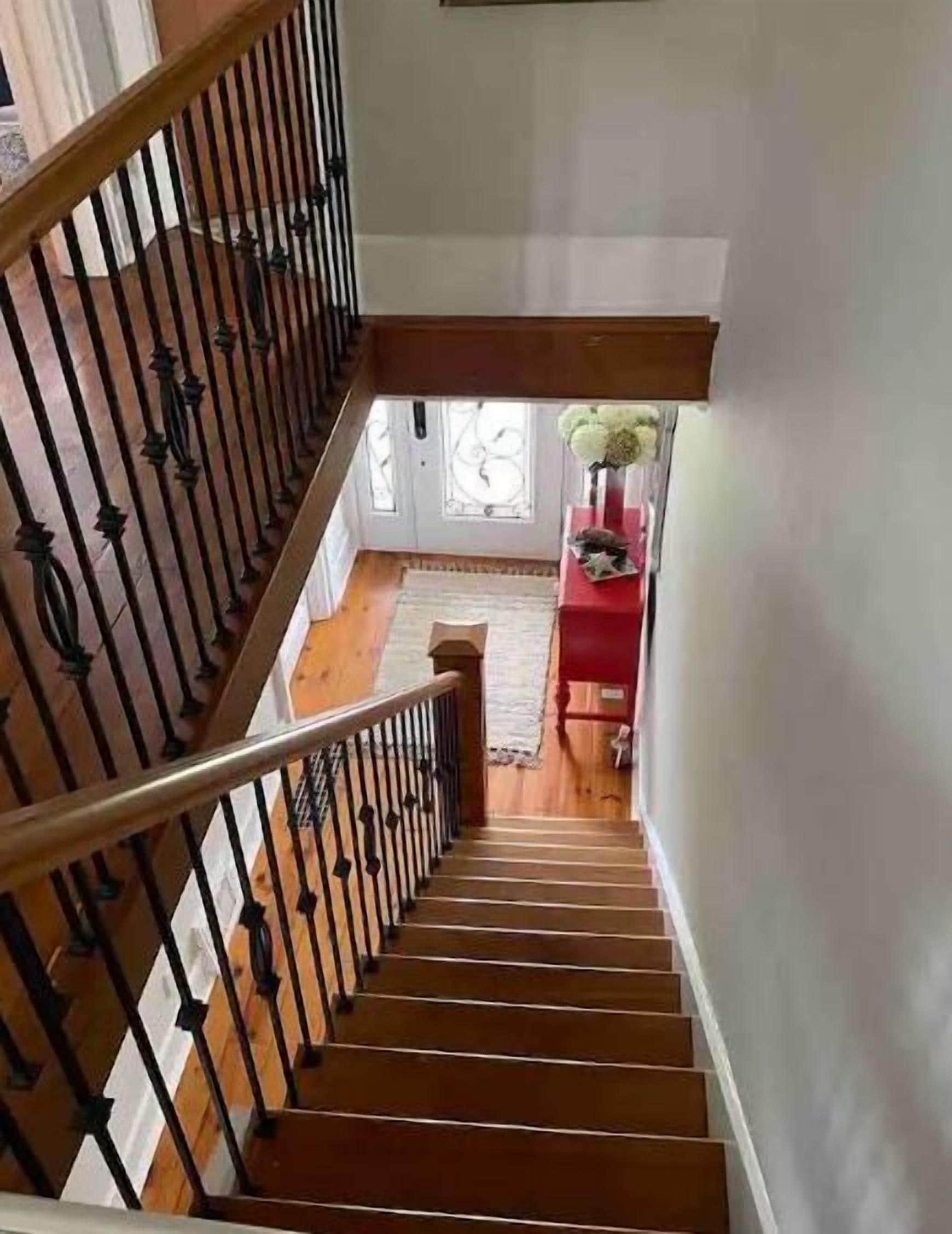 A wooden staircase with black railings leading to a room with a red table and a vase of flowers.