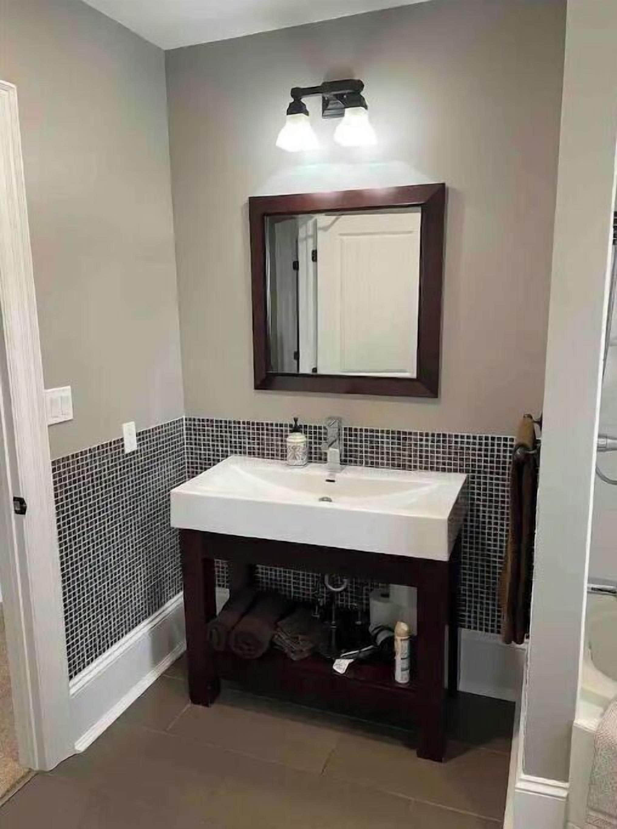 Une salle de bain avec un lavabo blanc, un meuble-lavabo en bois foncé et un miroir au-dessus.