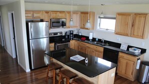 Una cocina moderna con armarios de madera, electrodomésticos de acero inoxidable, una isla central con taburetes y un ventanal que proporciona luz natural.