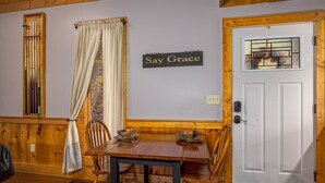 A dining area with a wooden table and chairs, a sign that says "Say Grace," and a white door with a stained glass window. - Fall Foliage! - Hot Tub with a View (Sevierville)