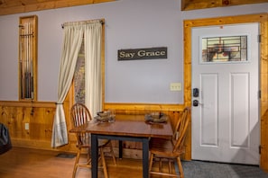 A dining area with a wooden table and chairs, a sign that says "Say Grace," and a white door with a stained glass window.