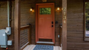 A wooden cabin entrance with a red door, numbered 2134, and a welcome mat. - Fall Foliage! - Hot Tub with a View (Sevierville)