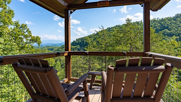 A wooden deck with two chairs and a table, overlooking a forested mountain area. - Fall Foliage! - Hot Tub with a View (Sevierville)