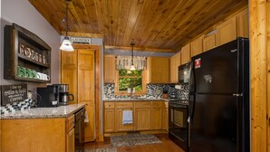 A kitchen with wooden cabinets, a black refrigerator, a coffee maker, and a laundry sign. - Fall Foliage! - Hot Tub with a View (Sevierville)