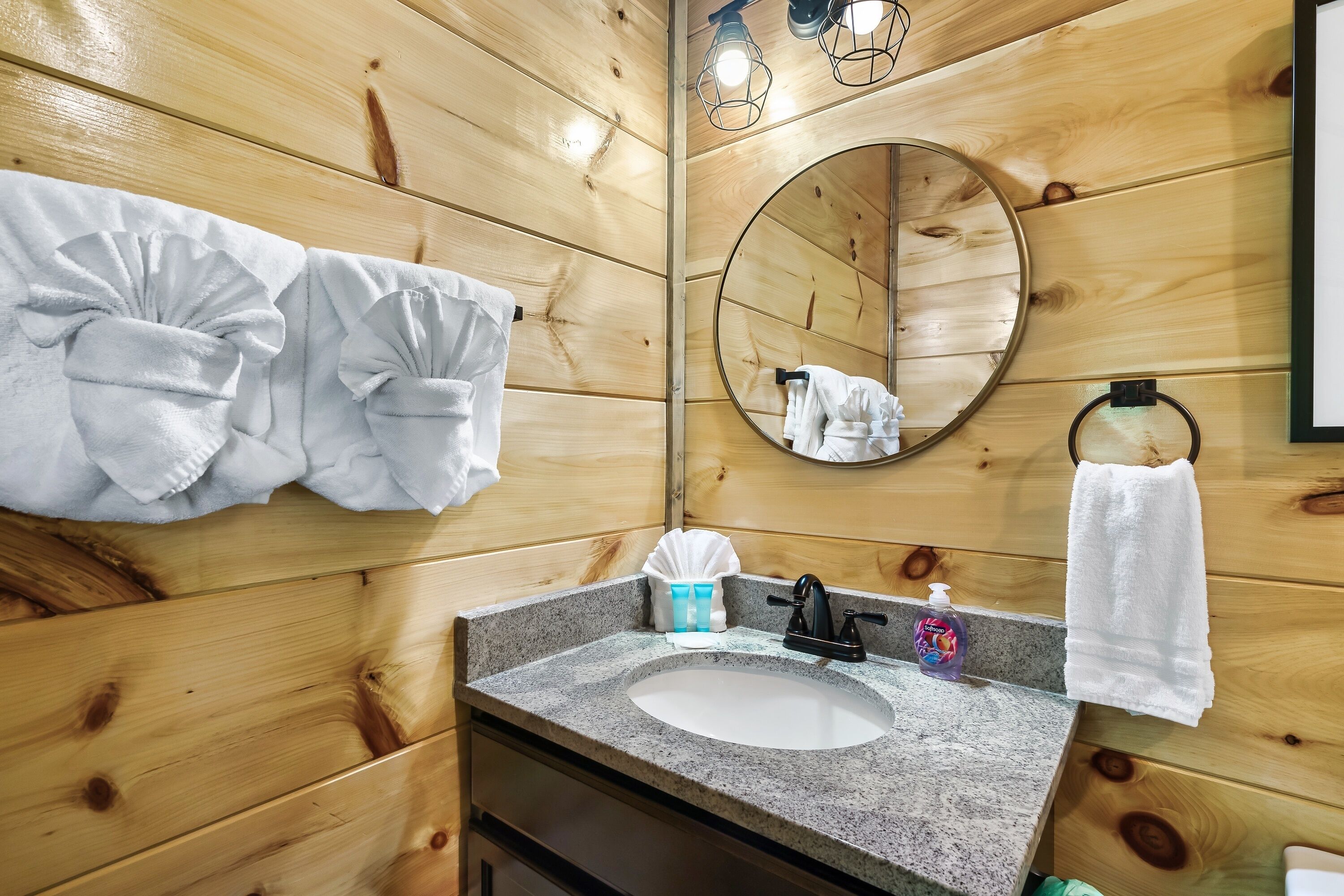 Un baño con paneles de madera, un lavamanos de granito, un espejo y toallas colgadas en la pared.