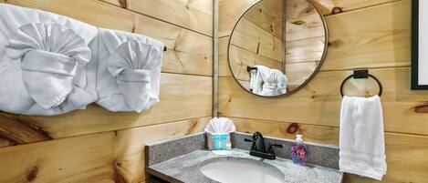 Un baño con paneles de madera, un lavamanos de granito, un espejo y toallas colgadas en la pared.