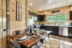 Un intérieur en bois avec une table à manger dressée pour six personnes, un coin cuisine et un panneau indiquant « CAFÉ ».