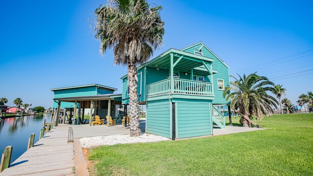 A turquoise building with a balcony, a dock, and a palm tree.