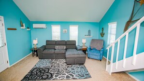 A living room with teal walls, a gray sectional sofa, a blue armchair, and a patterned rug.