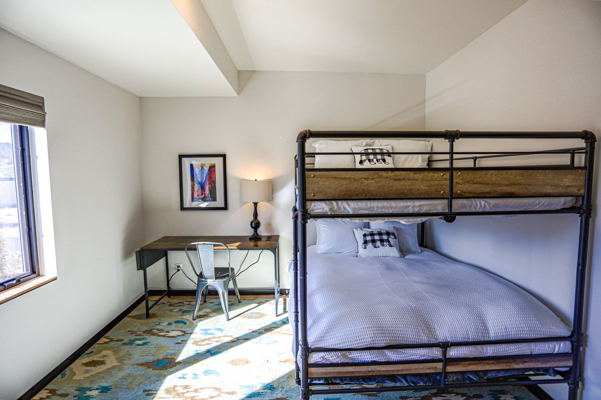 Un lit superposé avec un bureau et une chaise, une lampe et un tableau encadré au mur.