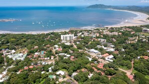 An aerial view of a coastal town with a beach, buildings, and greenery.