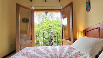 A bedroom with a bed, a nightstand, a window with an open door, and a view of greenery outside.