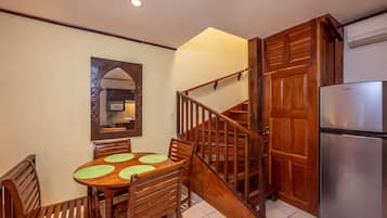 A dining area with a wooden table and chairs, a wooden staircase, and a stainless steel refrigerator.