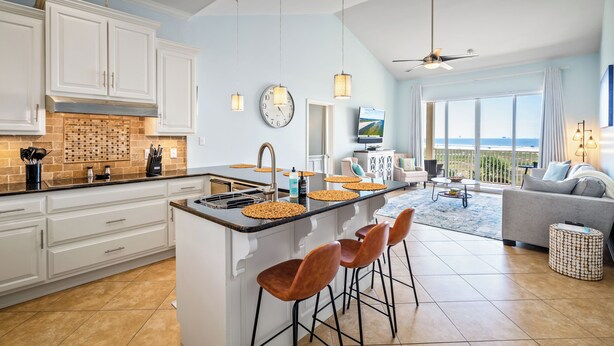 Una cucina moderna con mobili bianchi, un'isola centrale con sgabelli, un'ampia finestra vista e una ventola a soffitto.