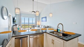 A modern kitchen with a central island, stainless steel appliances, pendant lighting, and a view to the outside.