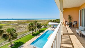 A balcony with a pool, outdoor furniture, and a view of the beach and ocean.