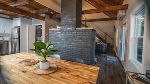 Una cocina moderna con una mesa de madera, una chimenea de ladrillo y una escalera que sube a otro nivel.