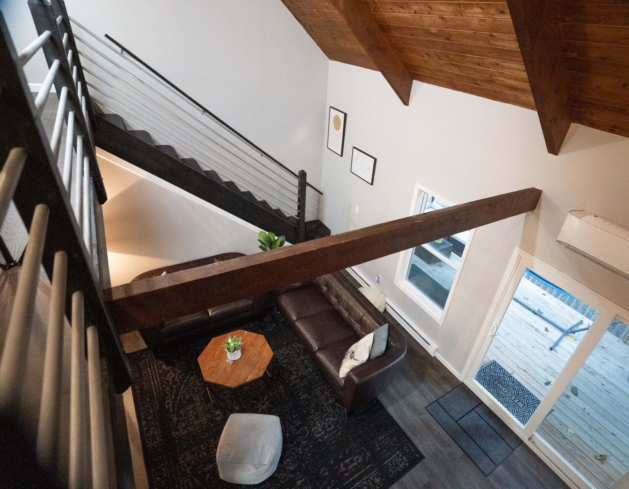 Eine Treppe mit Holengeländer führt zu einem Wohnbereich mit einer Couch, einem runden Couchtisch und einem kleinen Topfpflanzen.
