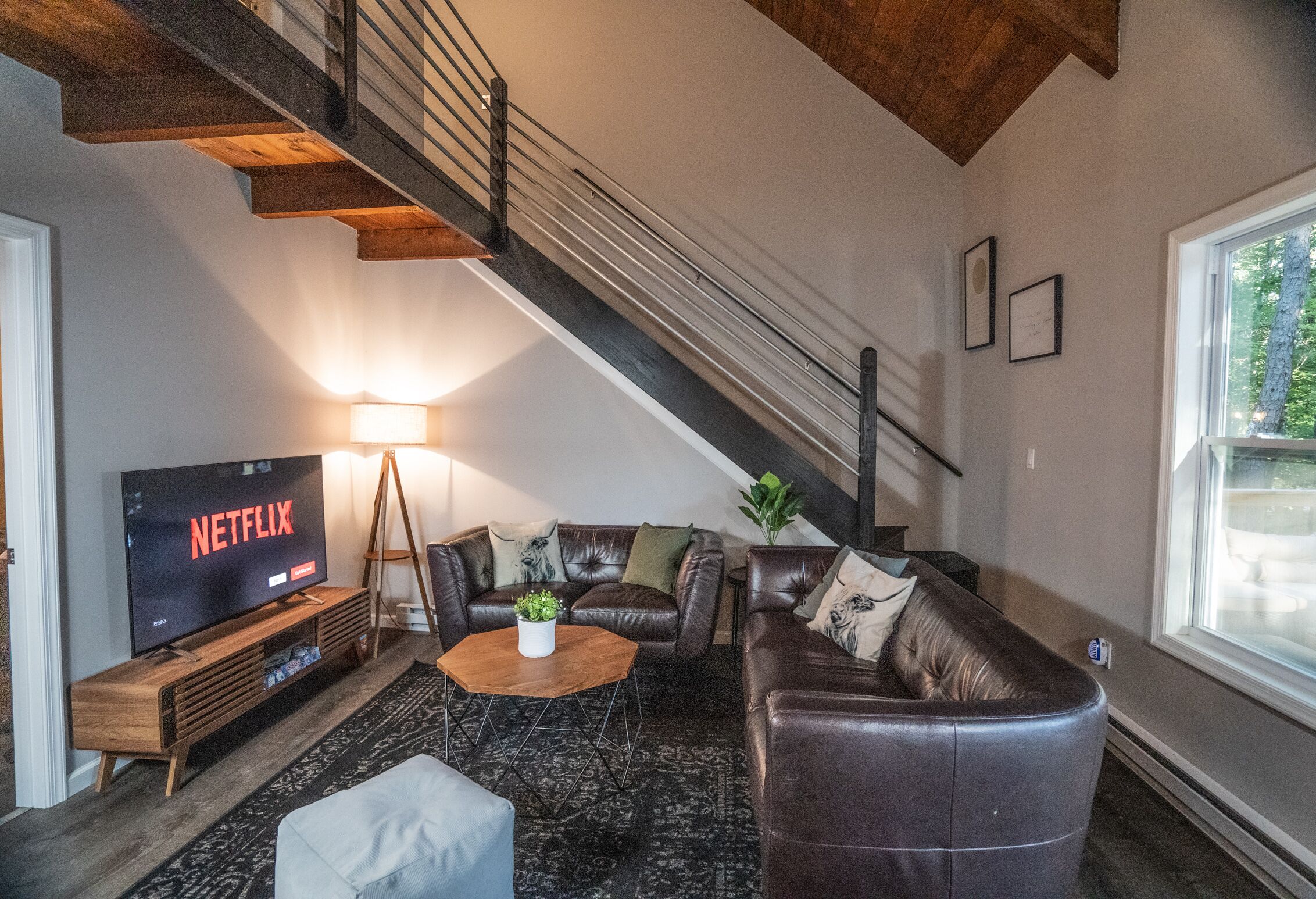 Ein modernes Wohnzimmer mit Treppe, Ledersofas, einem Holztisch und einem Fernseher, der 'NETFLIX' zeigt.