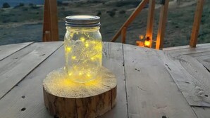 Et glas med lyskæder på en træstub på en terrasse med udsigt over havet og bakker.