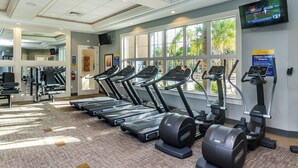 A fitness center with treadmills, elliptical machines, and a TV screen displaying sports.