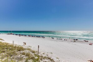 A beach with white sand and clear blue water. There are several umbrellas and beach chairs along the shore. - Fall and Winter 30-40% discounts! Located in the heart of Destin! (Destin)