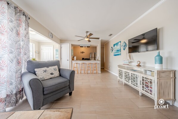 A modern living room with a grey sofa, a TV mounted on the wall, and a kitchen in the background.