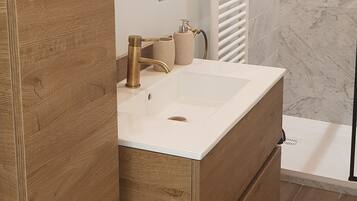 A modern bathroom with a wooden vanity, a round mirror, a white sink, and a shower area with marble walls.