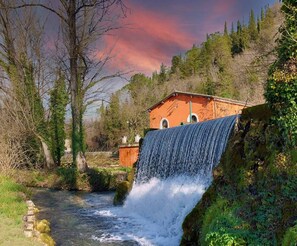 Un edificio rustico con una cascata di fronte, immerso tra alberi e un fiume.