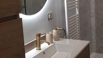Une salle de bain moderne avec un meuble-lavabo blanc, un miroir rond, une douche en verre et un porte-serviettes.