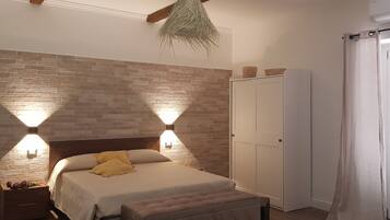 Ein Schlafzimmer mit einer ziegelmusternden Wand, einem Bett mit Kopfteil, zwei Wandleuchten, einem Kleiderschrank und einem Fenster mit Vorhängen.