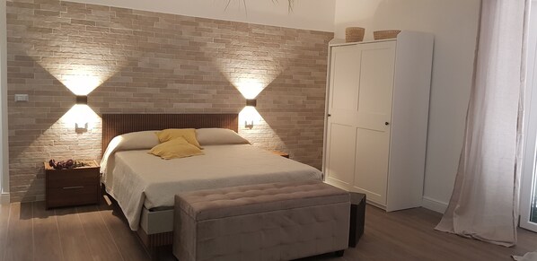 Una camera da letto con parete a mattoni, un letto con testiera in legno, due luci a parete, un armadio e una panca.