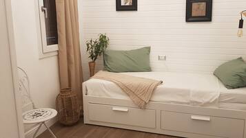 A small, neatly arranged bedroom with a single bed, a small table, and a chair.
