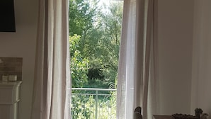 A room with a wooden ceiling, a dining table with chairs, and a view of greenery through sheer curtains.