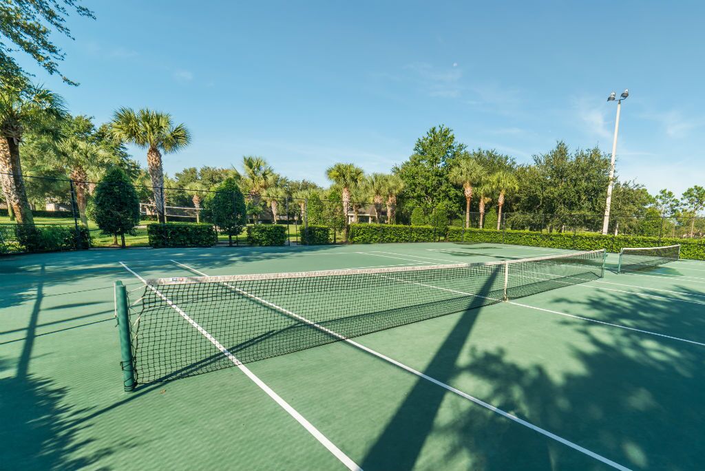 Una cancha de tenis con red, rodeada de árboles y cielo despejado.