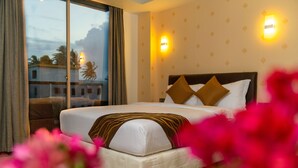 A hotel room with a large bed, two wall-mounted lights, and a view of palm trees outside. - Ari Grand Hotel & Spa (Dhangethi)