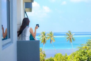 A person standing by a window overlooking a beach with palm trees and the ocean. - Ari Grand Hotel & Spa (Dhangethi)