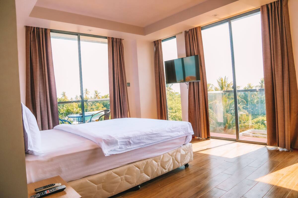 A hotel room with a bed, a TV, and large windows with curtains.