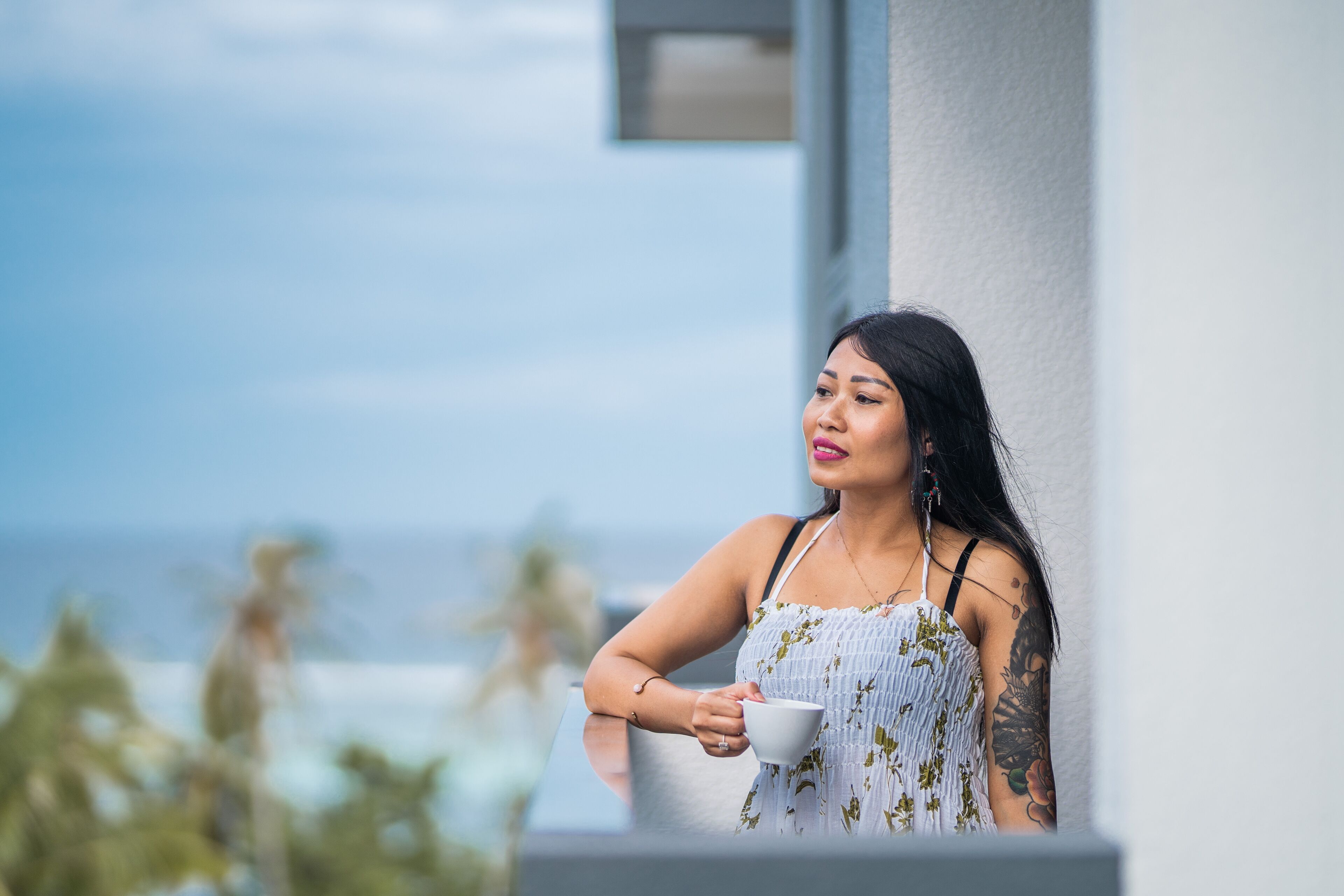 Une personne tenant une tasse sur un balcon avec vue sur l’océan.