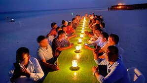 A group of people seated around a long table with candles on it, on a beach at night. - Ari Grand Hotel & Spa (Dhangethi)
