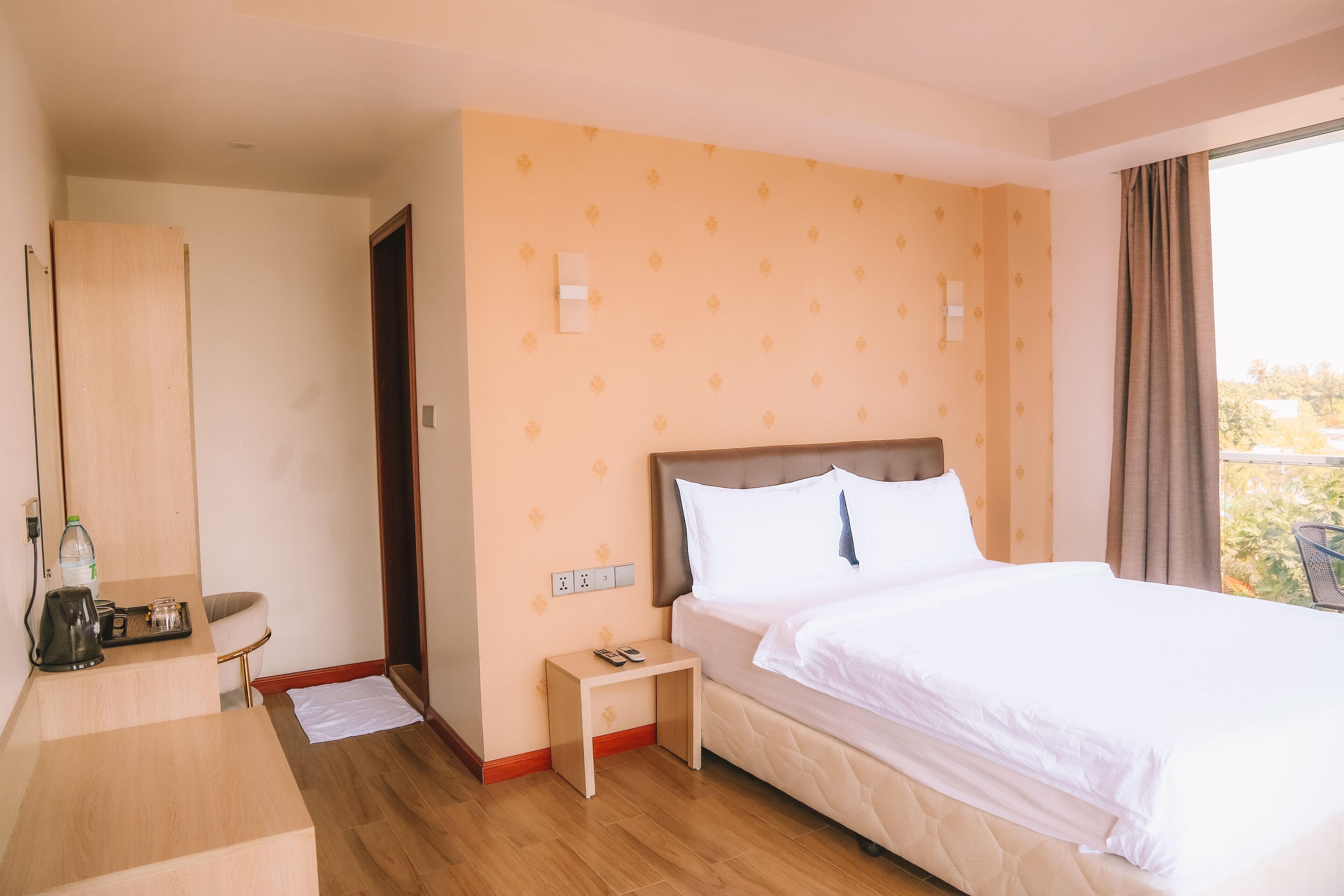 Una habitación de hotel con una cama, mesita de noche y una pequeña mesa con una botella y vasos.